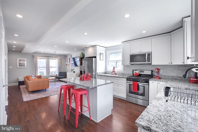 kitchen featuring appliances with stainless steel finishes, a breakfast bar, white cabinetry, a center island, and light stone countertops