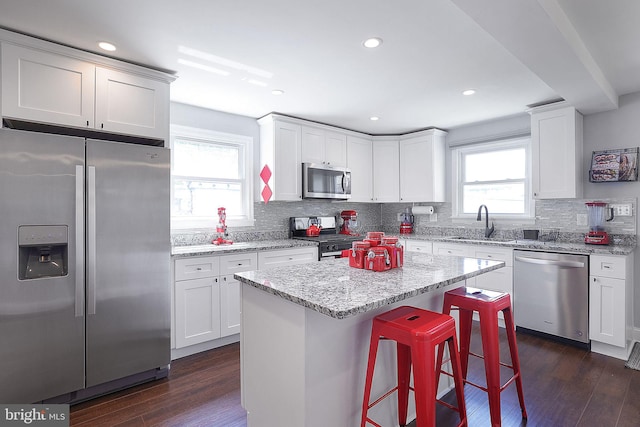 kitchen with stainless steel appliances, a kitchen island, sink, and white cabinets