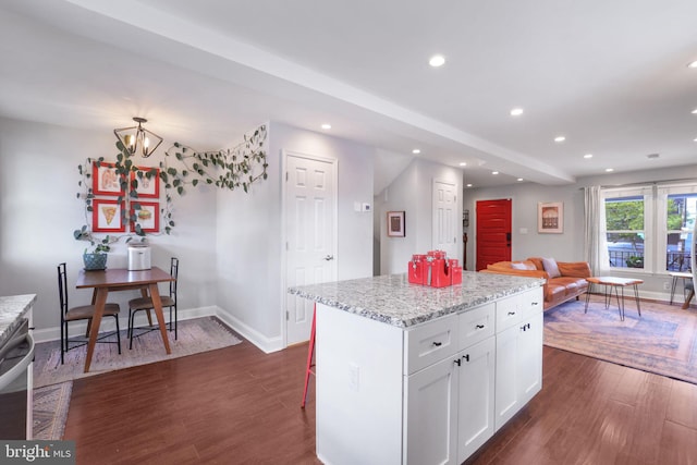 kitchen featuring a breakfast bar, white cabinetry, dark hardwood / wood-style floors, light stone countertops, and a kitchen island