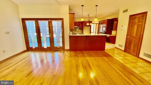 kitchen featuring stainless steel microwave, pendant lighting, light hardwood / wood-style floors, ventilation hood, and kitchen peninsula