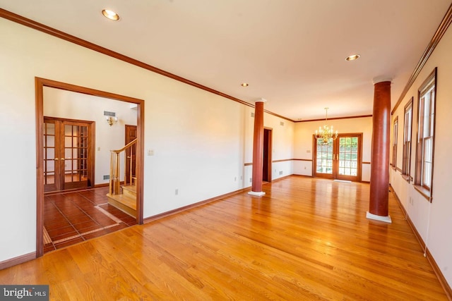 empty room with french doors, ornate columns, wood-type flooring, crown molding, and a chandelier