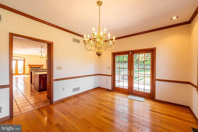 unfurnished room featuring an inviting chandelier, light hardwood / wood-style floors, french doors, and crown molding