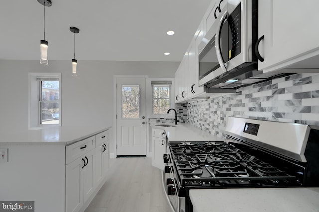 kitchen with appliances with stainless steel finishes, light countertops, hanging light fixtures, and white cabinetry