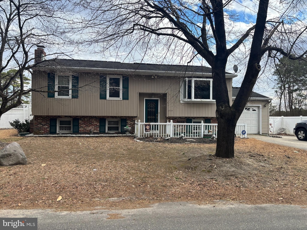 bi-level home with brick siding, a chimney, covered porch, a garage, and driveway