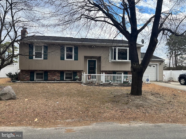 bi-level home with brick siding, a chimney, covered porch, a garage, and driveway