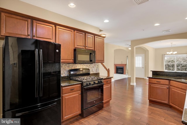 kitchen with tasteful backsplash, sink, hanging light fixtures, black appliances, and dark wood-type flooring