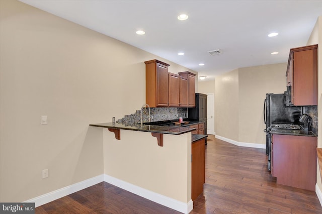 kitchen with dark wood-type flooring, kitchen peninsula, dark stone counters, and a kitchen bar