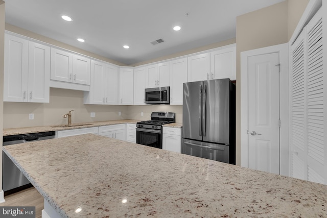 kitchen with white cabinetry, appliances with stainless steel finishes, sink, and light stone counters