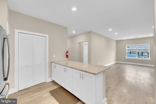 kitchen with light wood-type flooring, stainless steel fridge, kitchen peninsula, light stone countertops, and white cabinets