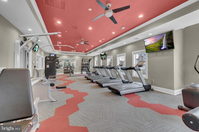 workout area featuring light colored carpet, ceiling fan, and a tray ceiling