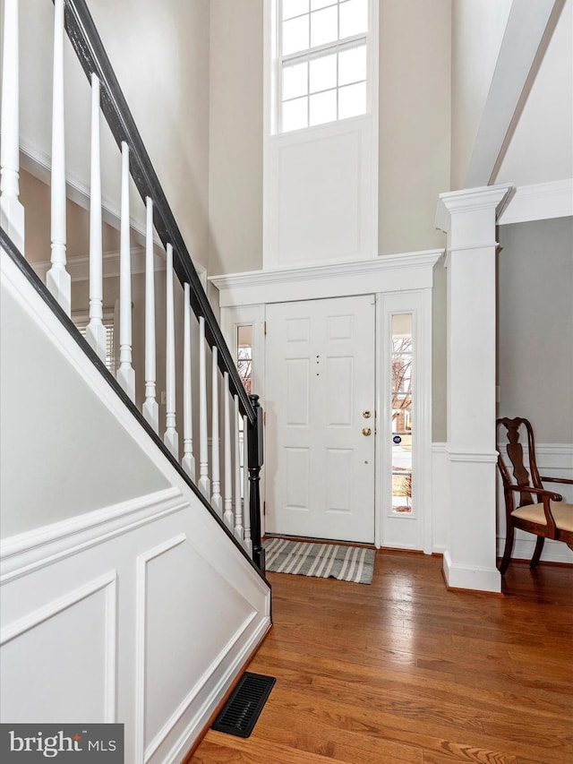 foyer entrance featuring visible vents, stairway, a towering ceiling, wood finished floors, and ornate columns