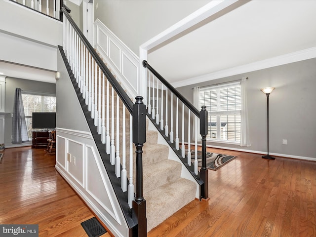 stairs with plenty of natural light, wood finished floors, and crown molding