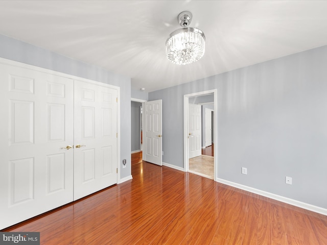 unfurnished bedroom with wood-type flooring, a chandelier, and a closet