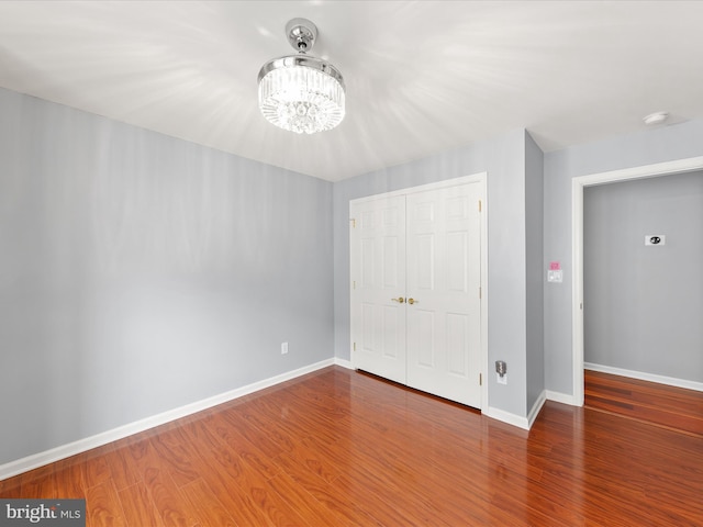 unfurnished bedroom featuring hardwood / wood-style floors, an inviting chandelier, and a closet