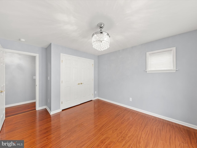 unfurnished bedroom featuring wood-type flooring, a closet, and a notable chandelier