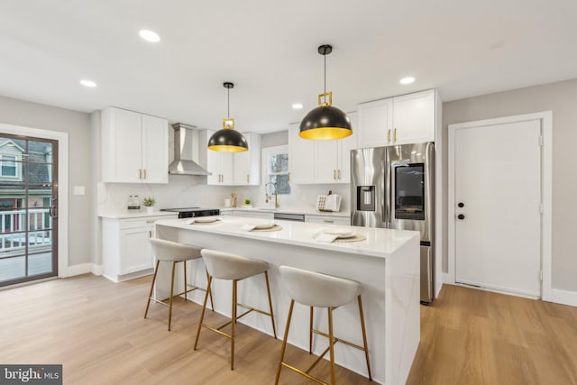 kitchen with a center island, stainless steel fridge with ice dispenser, white cabinetry, and wall chimney exhaust hood