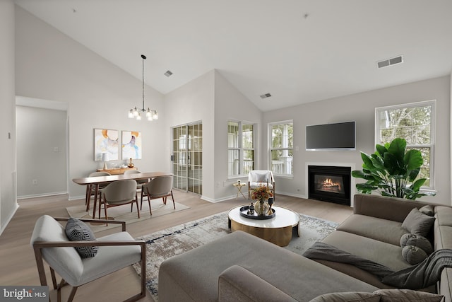 living area featuring light wood-style floors, a glass covered fireplace, a healthy amount of sunlight, and visible vents