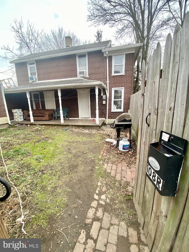 back of property featuring a chimney, fence, a porch, and brick siding