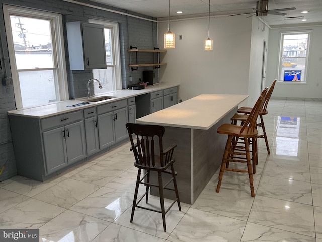 kitchen featuring a breakfast bar, hanging light fixtures, marble finish floor, light countertops, and a sink