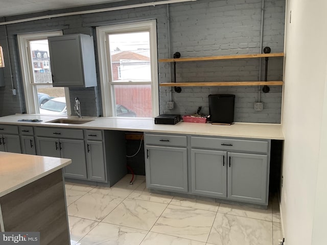 kitchen with a sink, light countertops, marble finish floor, and gray cabinetry