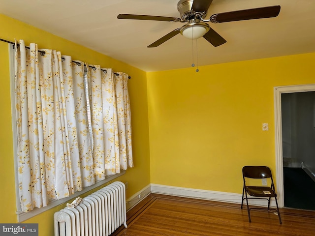 living area featuring radiator, a ceiling fan, baseboards, and wood finished floors