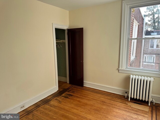 spare room featuring radiator heating unit, light wood-type flooring, and baseboards