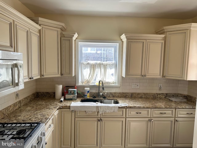 kitchen with white microwave, cream cabinets, a sink, and backsplash