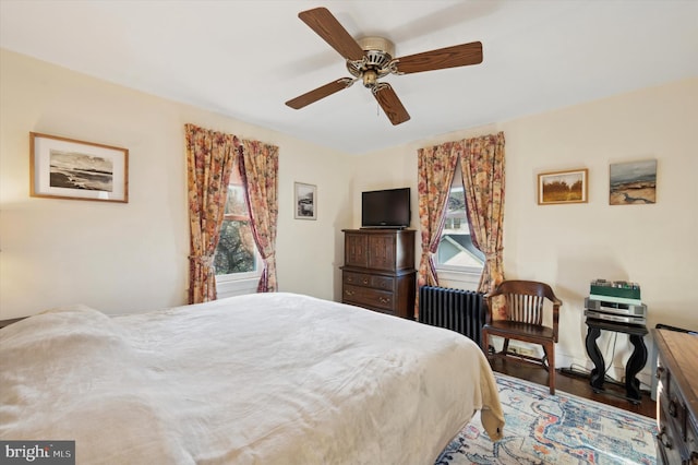 bedroom with multiple windows, radiator heating unit, ceiling fan, and wood-type flooring