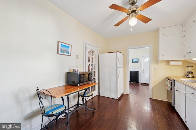 kitchen with dark wood-type flooring, appliances with stainless steel finishes, white cabinets, and radiator heating unit