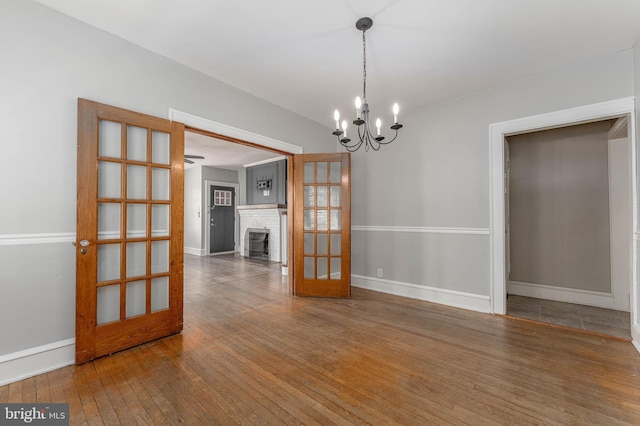 spare room with baseboards, wood-type flooring, an inviting chandelier, and a fireplace