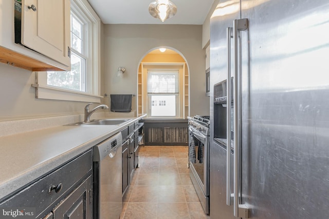 kitchen with light countertops, light tile patterned floors, arched walkways, stainless steel appliances, and a sink