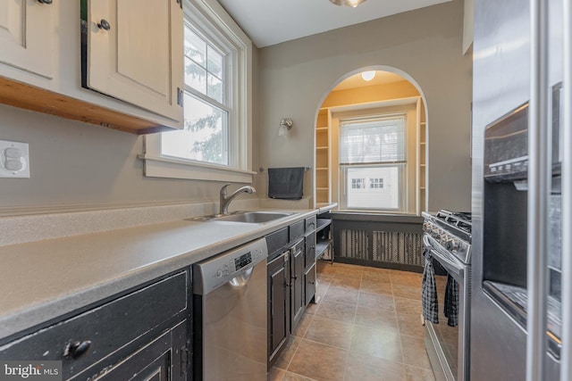 kitchen with light countertops, light tile patterned floors, dark cabinetry, stainless steel appliances, and a sink