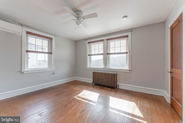 spare room with a ceiling fan, a wall mounted AC, hardwood / wood-style floors, radiator heating unit, and baseboards