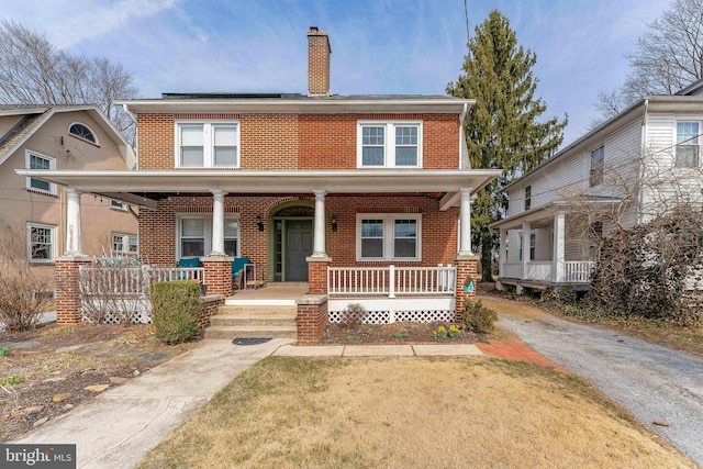 american foursquare style home featuring a front lawn, brick siding, covered porch, and a chimney