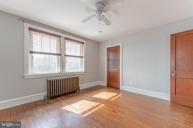 unfurnished room featuring baseboards, a ceiling fan, hardwood / wood-style floors, and radiator heating unit