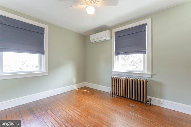 spare room with hardwood / wood-style floors, baseboards, a wall mounted AC, radiator heating unit, and ceiling fan