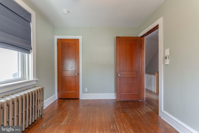 unfurnished bedroom with baseboards, radiator, and hardwood / wood-style flooring