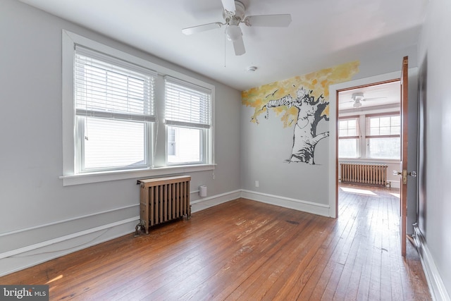 unfurnished room featuring radiator, baseboards, ceiling fan, and hardwood / wood-style flooring