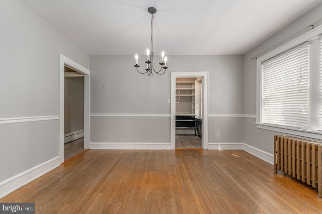 unfurnished dining area featuring radiator, baseboards, a baseboard radiator, an inviting chandelier, and hardwood / wood-style flooring