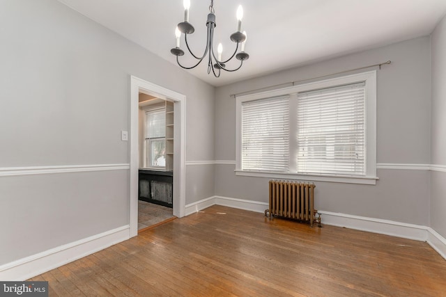 unfurnished room featuring baseboards, a notable chandelier, hardwood / wood-style floors, and radiator heating unit