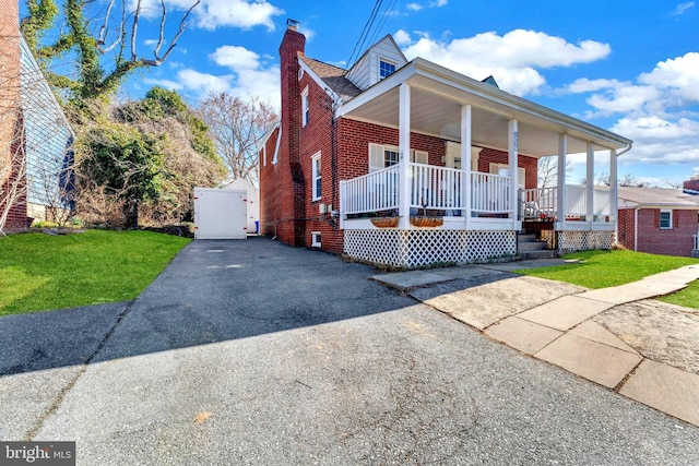 view of front of house featuring a porch, a front lawn, brick siding, and a chimney