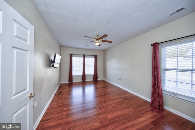 empty room with ceiling fan, wood finished floors, visible vents, and baseboards