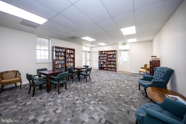 sitting room with bookshelves, carpet, a paneled ceiling, and baseboards