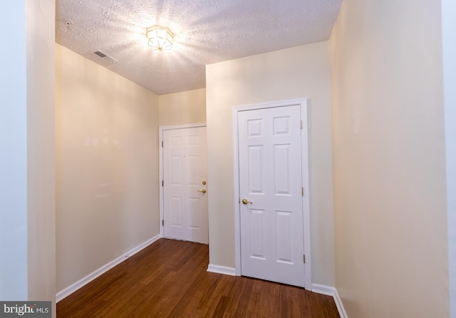 hall featuring baseboards, a textured ceiling, visible vents, and wood finished floors