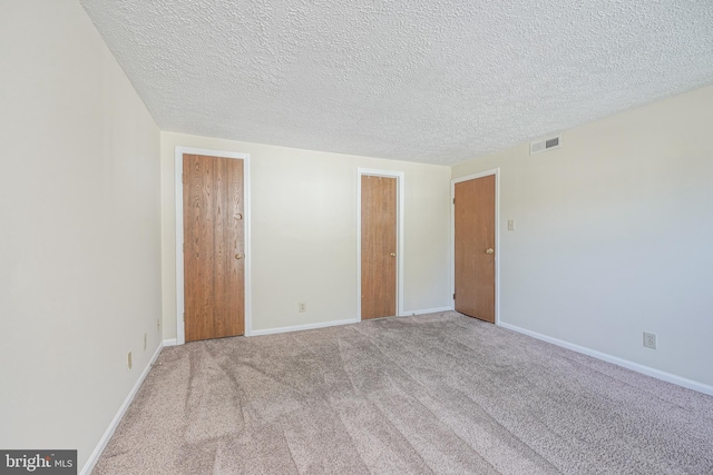 unfurnished bedroom featuring light carpet, a textured ceiling, visible vents, and baseboards