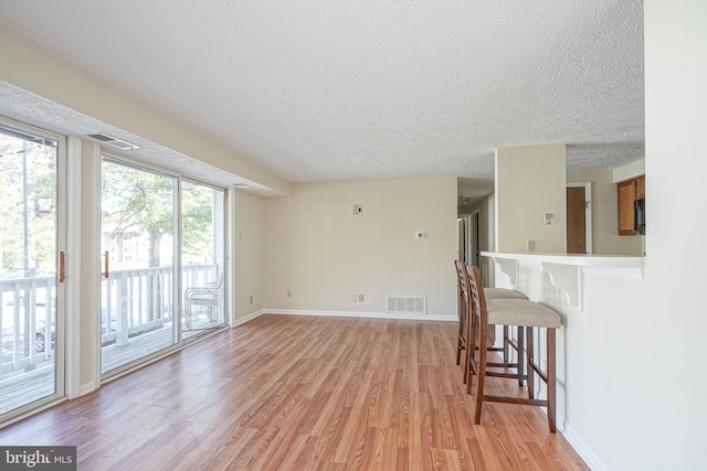 living area featuring a textured ceiling, light wood-style flooring, visible vents, and baseboards