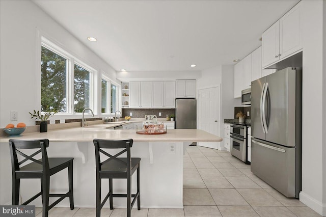 kitchen with stainless steel appliances, tasteful backsplash, white cabinets, a sink, and a peninsula