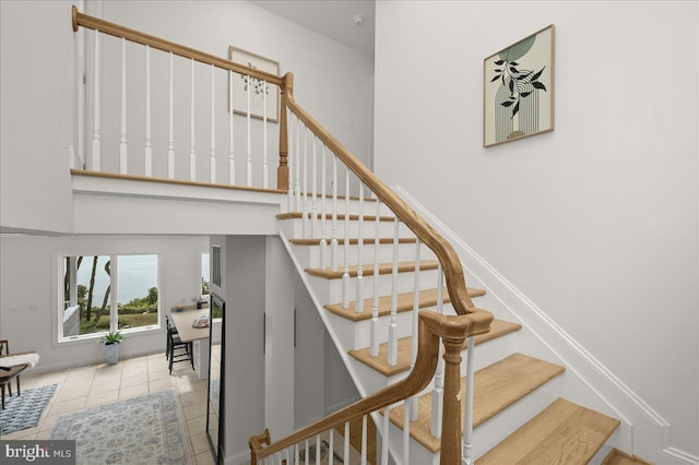 staircase featuring a towering ceiling, tile patterned flooring, and baseboards