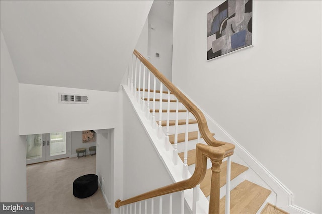 staircase featuring carpet flooring, a towering ceiling, visible vents, baseboards, and french doors