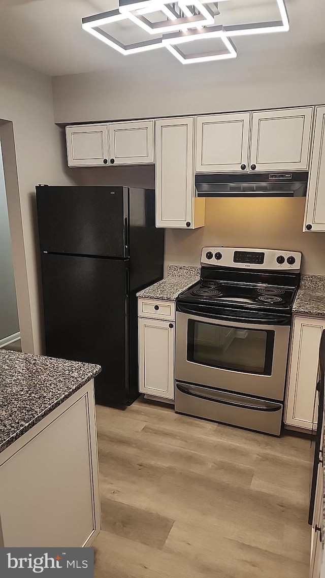 kitchen featuring under cabinet range hood, dark stone counters, white cabinets, freestanding refrigerator, and stainless steel electric range oven